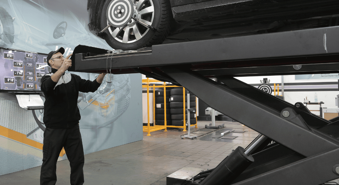car is lifted by the machine in the workshop , man , set of car tyres , screen with numbers