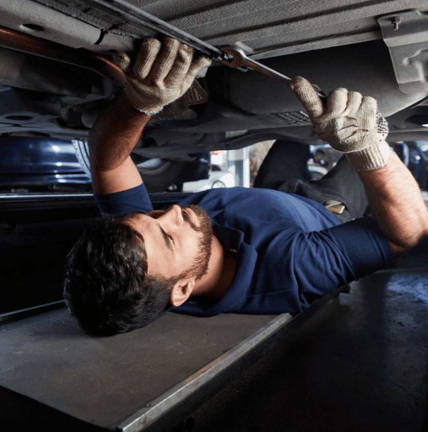 man wearing a navy t-shirt , gloves , grey pants , fixing the bottom of the car part