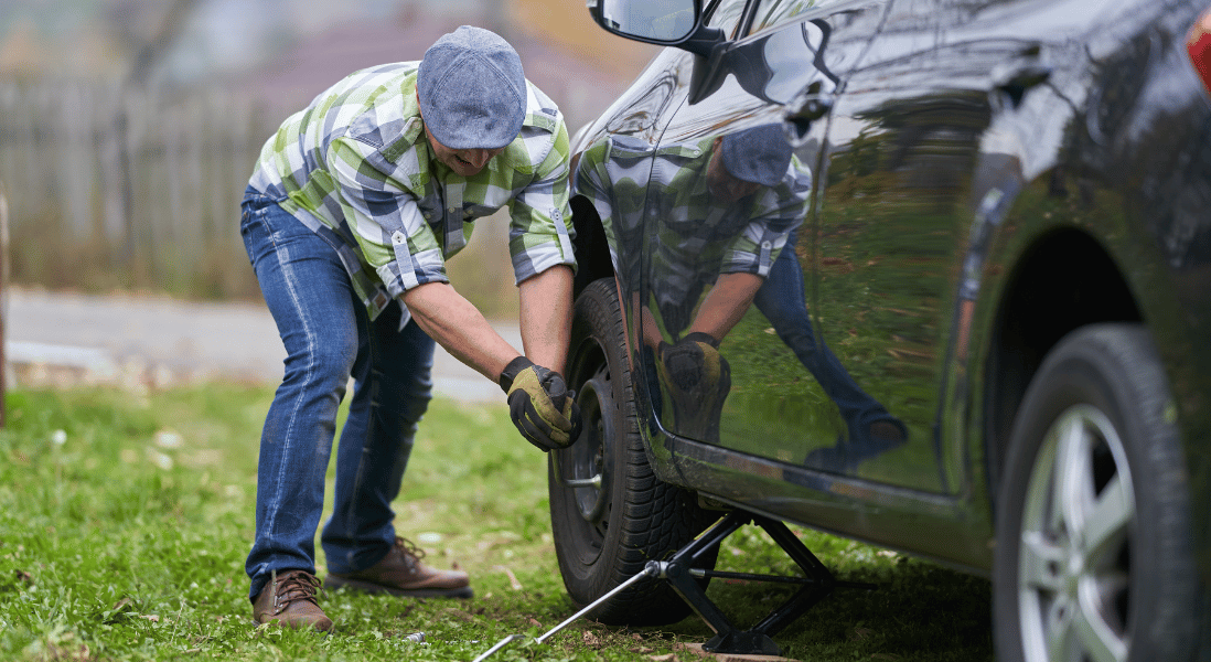 man safely parked his car next to the road to change a car tyre